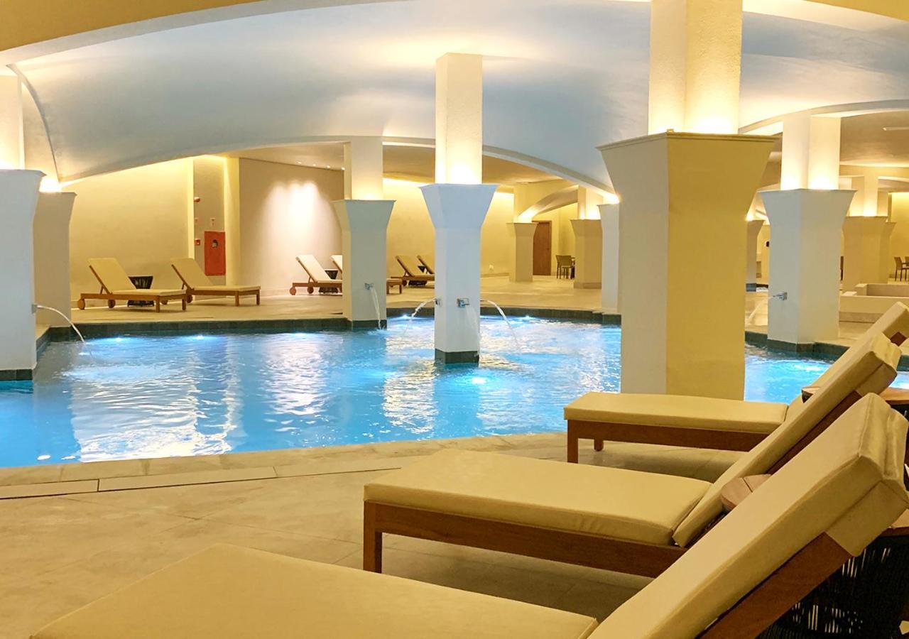 Buona Vitta Gramado Resort & Spa By Gramado Parks Exterior foto The photo shows an indoor spa or relaxation area with a tranquil atmosphere. There is a large swimming pool with clear blue water, illuminated by soft lighting. Surrounding the pool are several comfortable lounge chairs. The architecture features ele