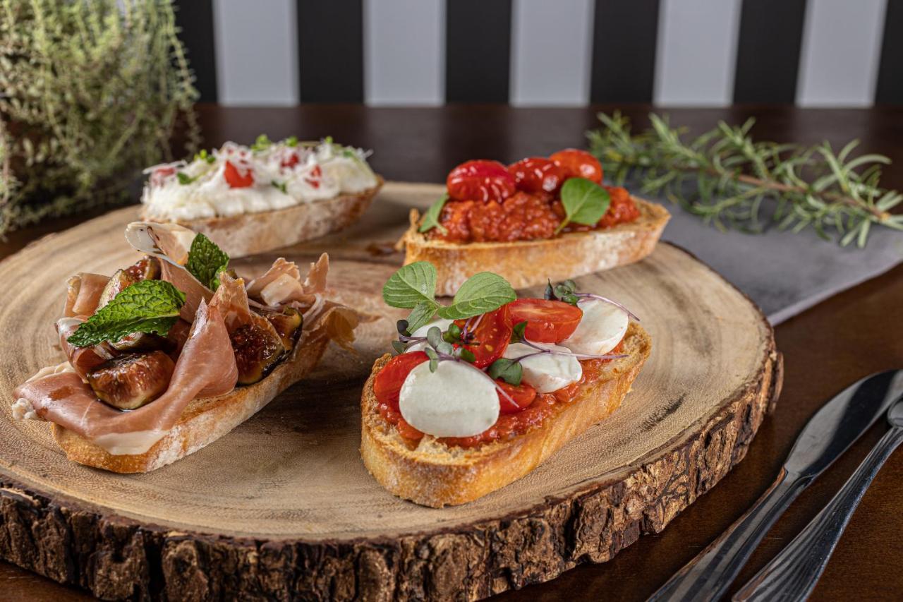 Buona Vitta Gramado Resort & Spa By Gramado Parks Exterior foto The photo displays a wooden serving platter featuring four different types of bruschetta. Each piece of bruschetta is topped with various ingredients:

1. The top left has a creamy spread, possibly cheese or ricotta, garnished with fresh herbs and sm