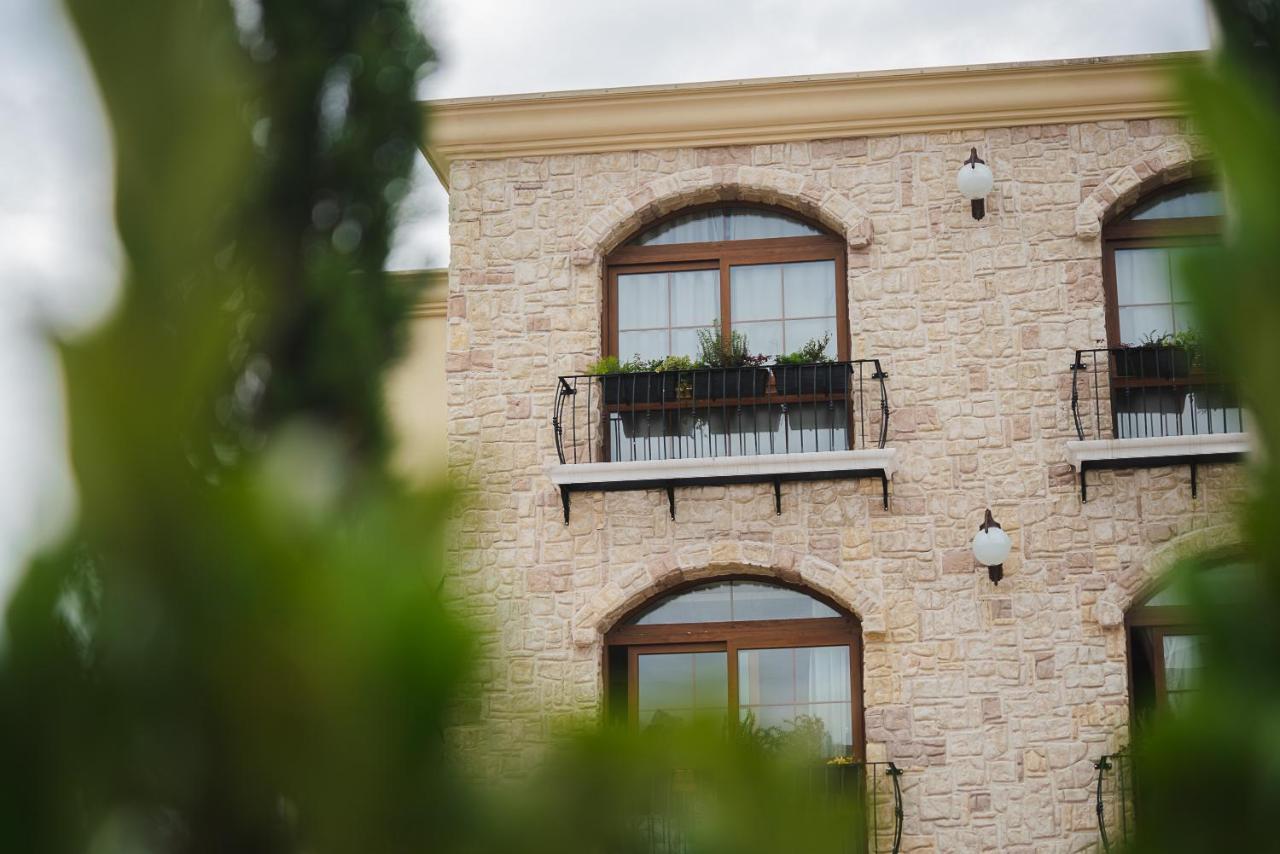 Buona Vitta Gramado Resort & Spa By Gramado Parks Exterior foto The photo depicts a stone building with a textured exterior. It features several windows with wooden frames. Each window has a small balcony adorned with decorative plants. There are also wall-mounted light fixtures flanking the windows. In the foreg