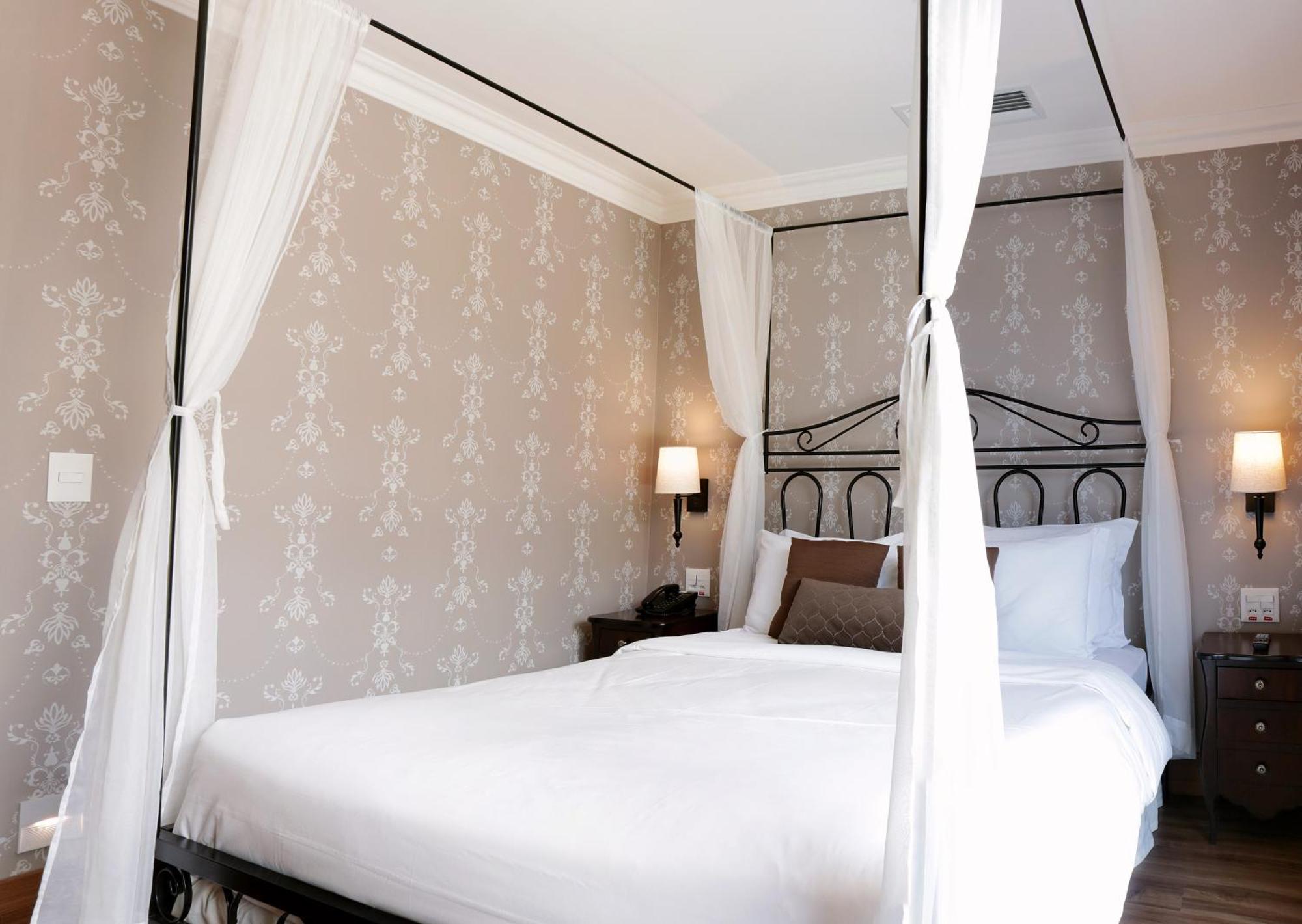 Buona Vitta Gramado Resort & Spa By Gramado Parks Exterior foto The photo shows a elegantly decorated bedroom featuring a four-poster bed with white drapes. The bed is made with white linens and has some brown accent pillows. The walls are adorned with a subtle floral pattern, and there are two bedside lamps prov